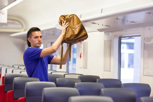 Young man putting luggage into overhead locker at train — Stock Photo, Image