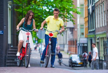 Amsterdam 'ın eski sokaklarında bisiklete binen mutlu beyaz bir çift.