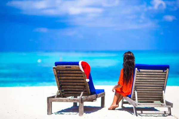 Concetto natalizio: lettini da spiaggia con Santa Hat rosso e bella ragazza durante le vacanze tropicali — Foto Stock