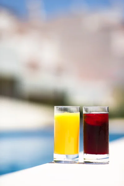 Two glasses of cherry and orange juice by the pool in summer time — Stock Photo, Image