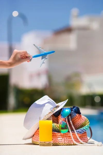 Colorful beach bag, glass of juice, straw hat and airplane model in female hand on summer vacation — Stock Photo, Image