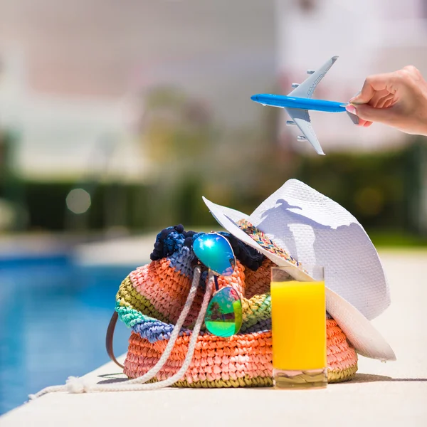 Colorful beach bag, glass of juice, straw hat and airplane model in female hand on summer vacation — Stock Photo, Image
