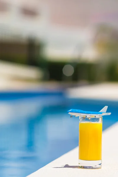 Verano y concepto de viaje: modelo de avión pequeño y vaso de jugo de naranja cerca de la piscina — Foto de Stock