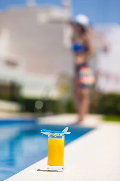 Lato i podróży koncepcja: mały samolot model i kieliszek soku pomarańczowego, w pobliżu basen — Zdjęcie stockowe