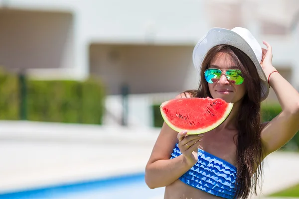 Mujer joven en sombrero y gafas de sol con sandía relajante cerca de la piscina — Foto de Stock