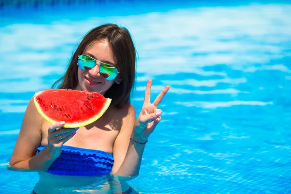 Young happy girl in sunglasses with watermelon relaxing in swimming pool