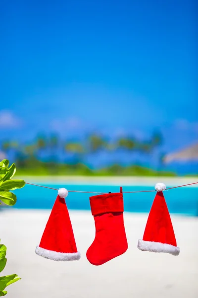 Red Santa hats and Christmas stocking hanging on tropical beach — Stock Photo, Image