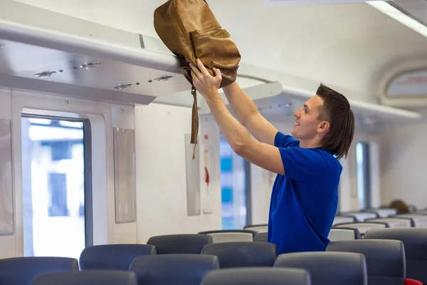 Young man putting luggage into overhead locker at airplane — Stock Photo, Image