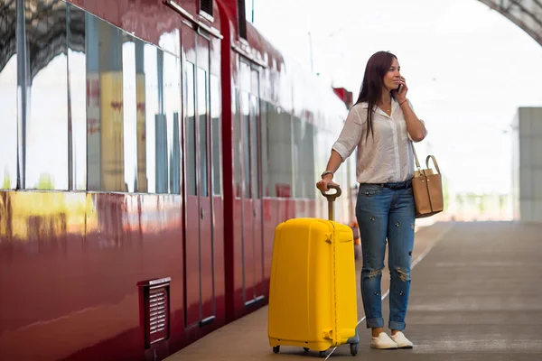 Ung kvinna med bagage talar av cellphone på en station — Stockfoto