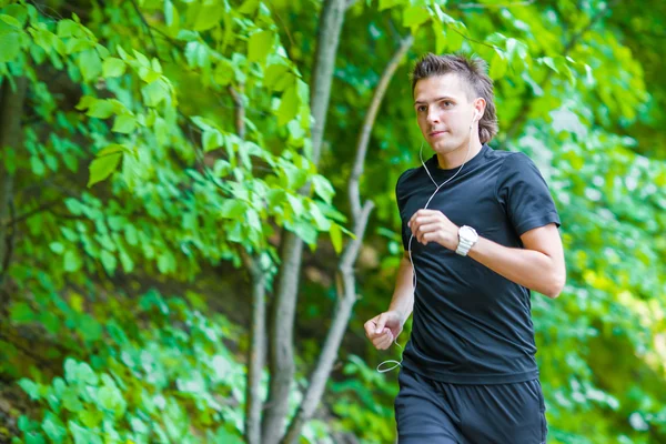 Deportivo en forma joven hombre corriendo mientras escucha música en el teléfono inteligente al aire libre —  Fotos de Stock