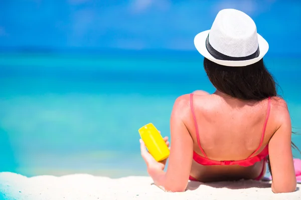 Mulher bonita segurando um protetor solar deitado na praia tropical — Fotografia de Stock