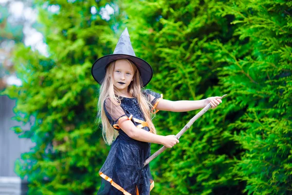 Urocza dziewczynka w kostiumie czarownicy z miotłą na zewnątrz w Halloween — Zdjęcie stockowe