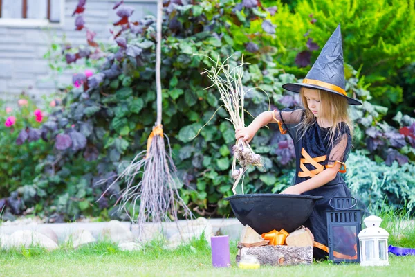 Adorable little girl wearing witch costume with broom on Halloween outdoors