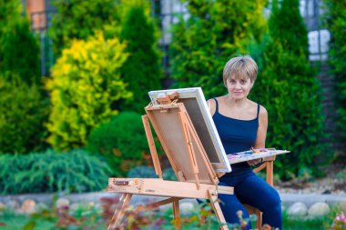 Mutlu kadın sıcak bir günde bir şövale resmi boyama