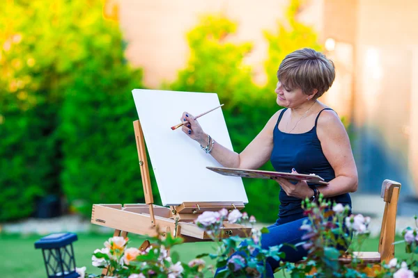 Happy woman painting a picture on an easel on a warm day