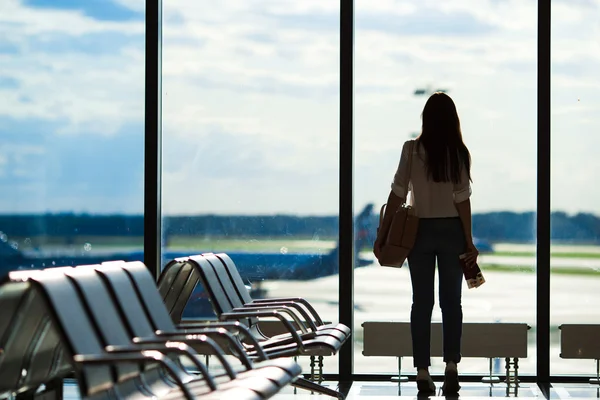 Jonge vrouw in de buurt van venster in een luchthaven lounge wachten voor vlucht vliegtuigen — Stockfoto