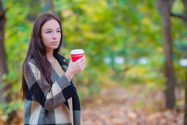 Podzimní koncepce - krásná žena pije kávu v podzimním parku pod podzimní listí — Stock fotografie