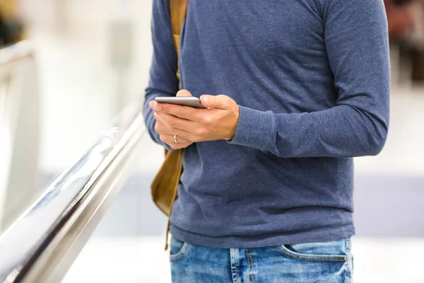 Hombre con mochila sosteniendo teléfono celular en el aeropuerto esperando el vuelo —  Fotos de Stock