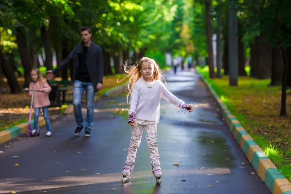 Kleines Mädchen mit Vater und Schwester auf Rollschuhen im Park — Stockfoto