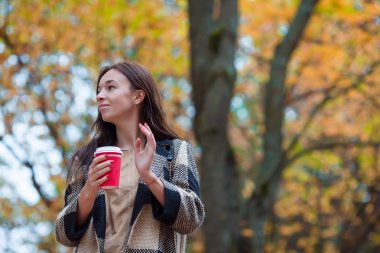 Sonbahar konsepti: Sonbahar parkında sonbahar yaprakları altında kahve içen güzel bir kadın.