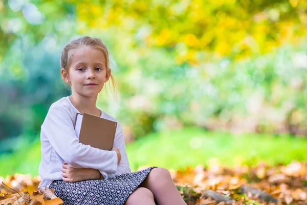 Adorável menina inteligente pouco com livro em dau outono bonito ao ar livre — Fotografia de Stock