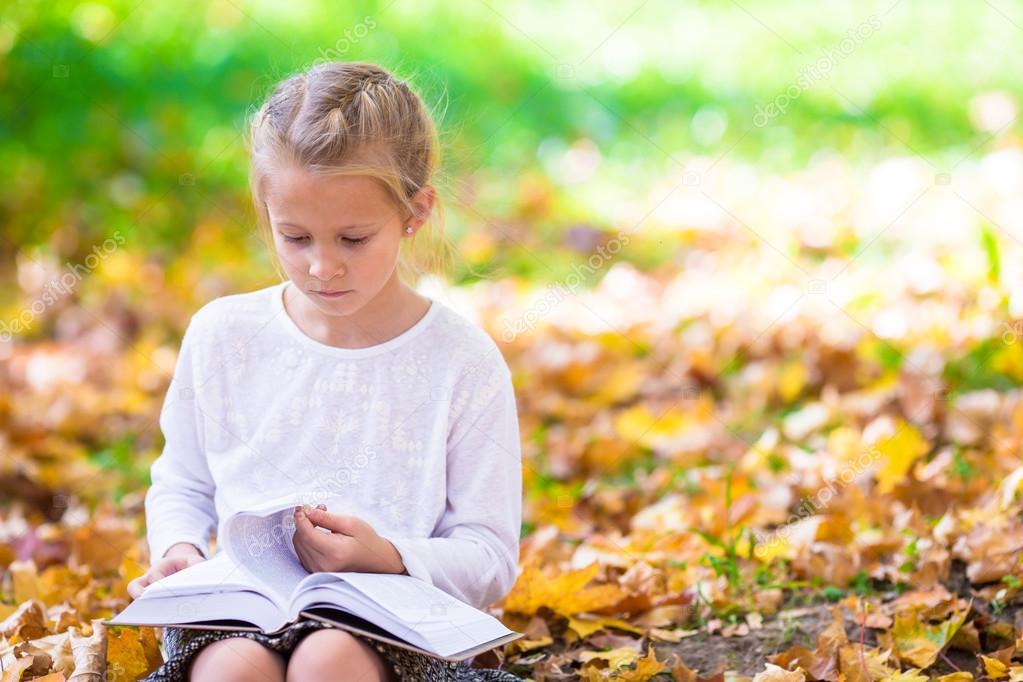 Adorable little girl reading a book in beautiful autumn park