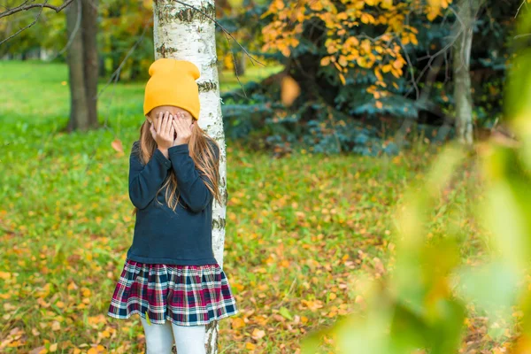 Liten flicka som leker kurragömma nära träd i höst park — Stockfoto