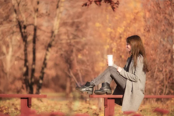 Jesienna koncepcja - piękna kobieta pijąca kawę w jesiennym parku pod jesiennymi liśćmi — Zdjęcie stockowe