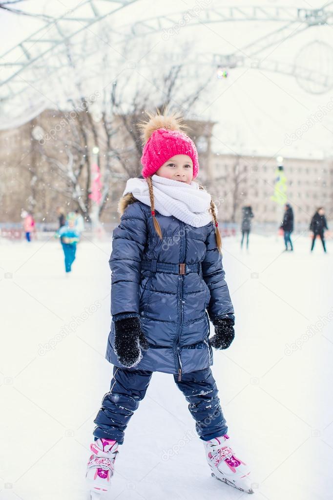 Adorable fashion little girl skating on the ice rink outdoors