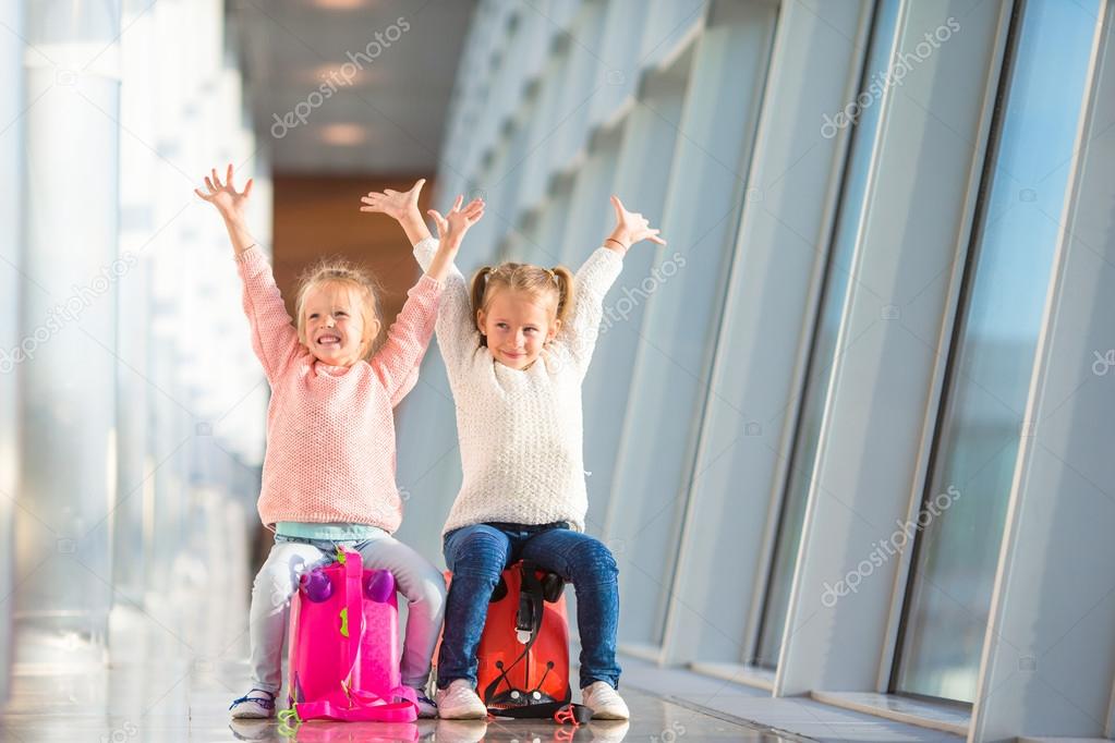 Adorable little girls having fun in airport sitting on suitcase waiting for boarding