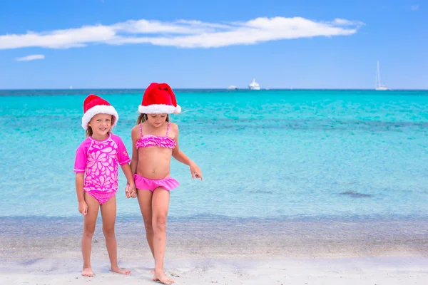 Kleine süße Mädchen in Weihnachtsmützen, die während der Weihnachtsferien am Strand Spaß haben — Stockfoto