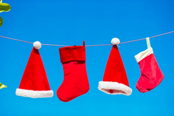 Red Santa Hats and Christmas stocking between palm trees on white beach — Stock Photo, Image
