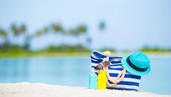 蓝色的袋子，稻草帽子、 墨镜和防晒霜瓶在白色的沙滩上 — 图库照片