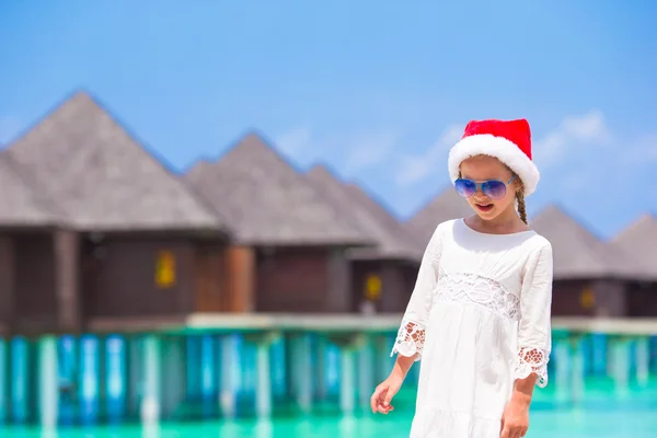 Kleines entzückendes Mädchen mit rotem Weihnachtsmann-Hut am weißen Strand — Stockfoto