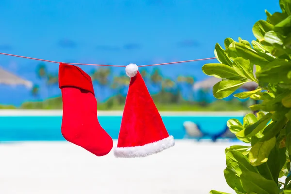 Roter Weihnachtsmann und Weihnachtsstrumpf zwischen Palmen am weißen Strand — Stockfoto