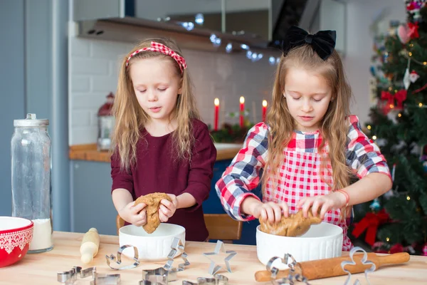 Маленькие счастливые девочки пекут пряничное печенье на Рождество на домашней кухне — стоковое фото