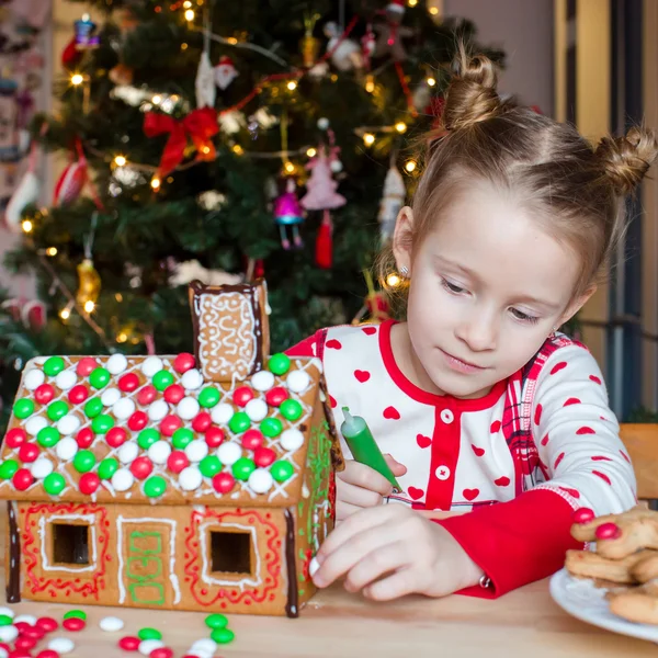 Kleines entzückendes Mädchen dekoriert Lebkuchenhaus zu Weihnachten — Stockfoto