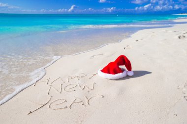 Mutlu yeni yıl plaj beyaz kum kırmızı Noel Baba şapkası ile yazılı