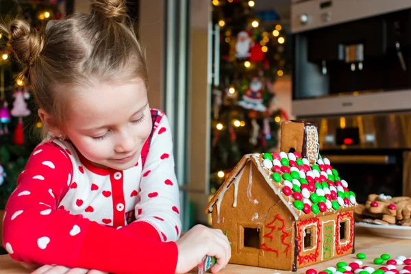 Kleines entzückendes Mädchen dekoriert Lebkuchenhaus zu Weihnachten — Stockfoto