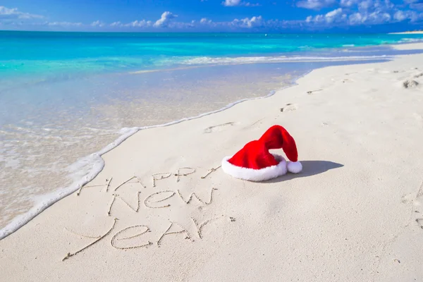 Felice anno nuovo scritto sulla spiaggia di sabbia bianca con cappello rosso Babbo Natale — Foto Stock