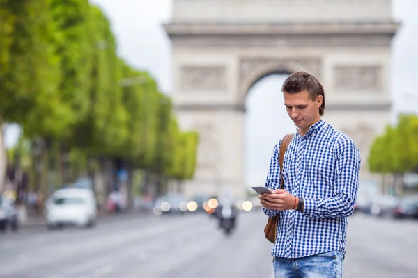 Ung kaukasisk mann som holder en telefon om Champs Elysees i Paris – stockfoto