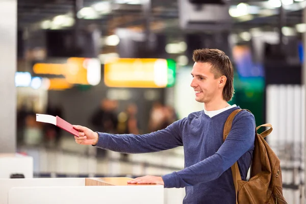 Young man with passports and boarding tickets at the front desk in airport — Stock Photo, Image