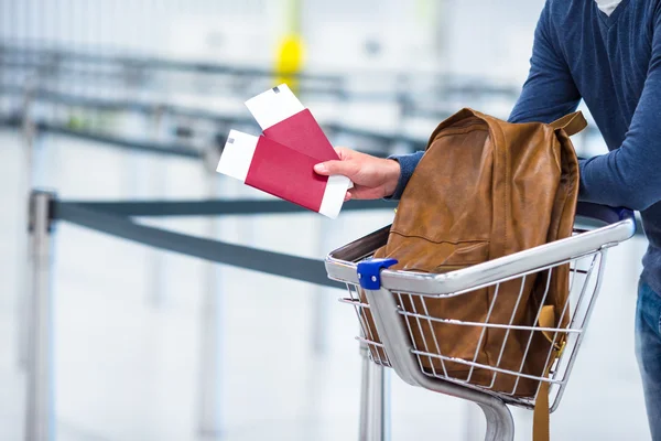 Young man with passports and boarding passes at the front desk at airport waiting for flight — Stock Photo, Image