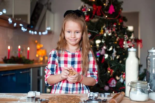 Entzückendes Mädchen, das an Heiligabend zu Hause Weihnachtsplätzchen backt. Weihnachtsbaum und Lichter im Hintergrund. — Stockfoto