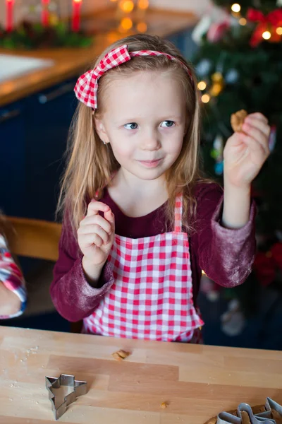 Entzückendes Mädchen, das an Heiligabend Weihnachtsplätzchen backt. Weihnachtsbaum und Lichter im Hintergrund. — Stockfoto