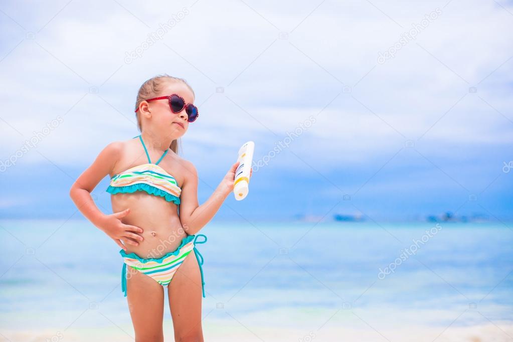 Little adorable girl applying sun cream during beach vacation
