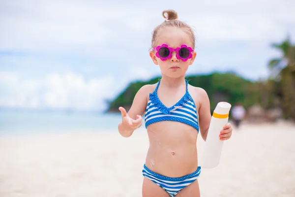 Little adorable girl with suntan lotion bottle on white beach — Stock Photo, Image