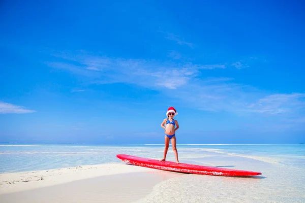 サンタ帽子練習サーフィン休暇中にサーフボードの位置に愛らしい少女 — ストック写真