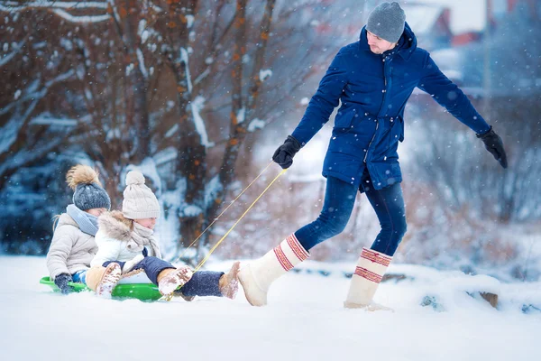 As meninas gostam de andar de trenó. O pai a passear com as suas filhas adoráveis. Férias em família na véspera de Natal ao ar livre — Fotografia de Stock