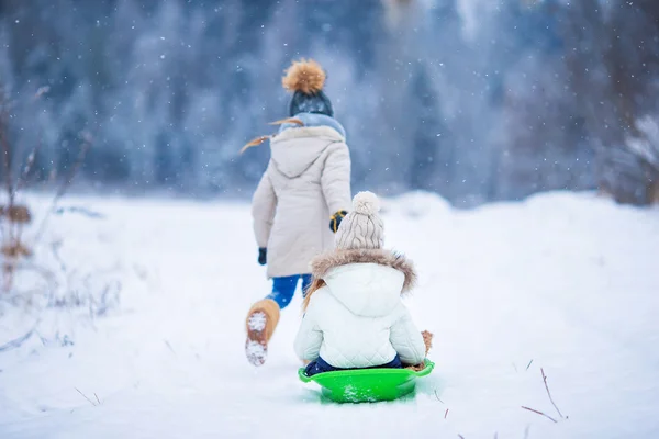 Little adorable girls enjoy a sleigh ride. Child sledding. Children play outdoors in snow. Family vacation on Christmas eve outdoors — Stock Photo, Image